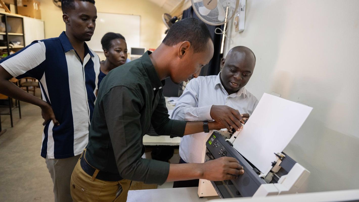 A photo of Abdulkadir Mohamed Abdullahir examines one of the braille machines during a training on braille production and digital inclusion at KyU Hi-Techn Center in Kampala, Uganda.