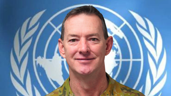 A headshot of a man in military uniform standing in front of the UN logo
