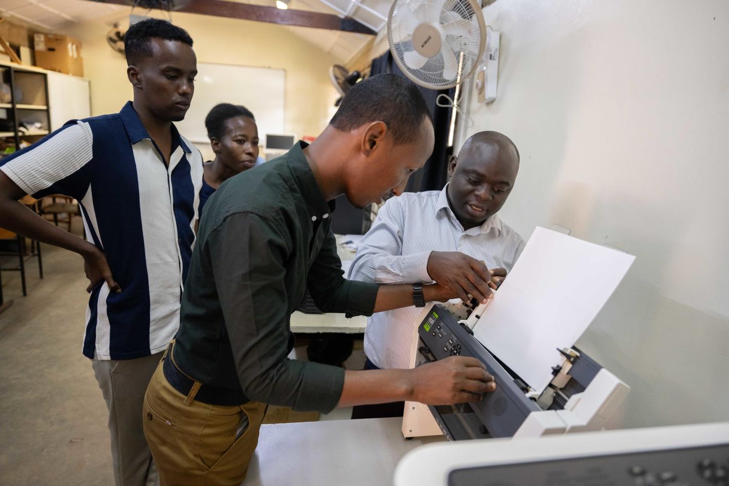 A photo of Abdulkadir Mohamed Abdullahir examines one of the braille machines during a training on braille production and digital inclusion at KyU Hi-Techn Center in Kampala, Uganda.