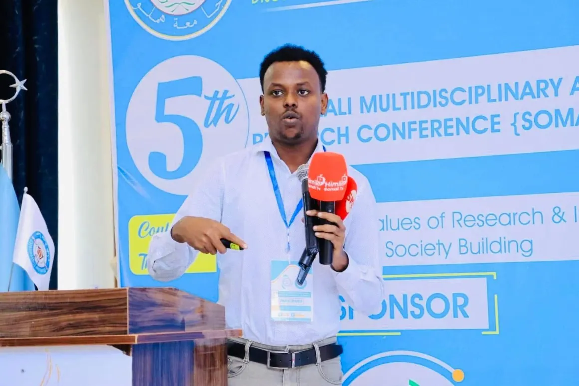Abdishakur Abdirahman in front of a banner of the 5th Somali Multidisciplinary Research Conference Abdishakur Abdirahman in front of a banner of the 5th Somali Multidisciplinary Research Conference